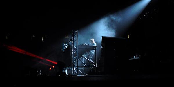 Diplo plays electronic dance music on stage under a single white spot light.